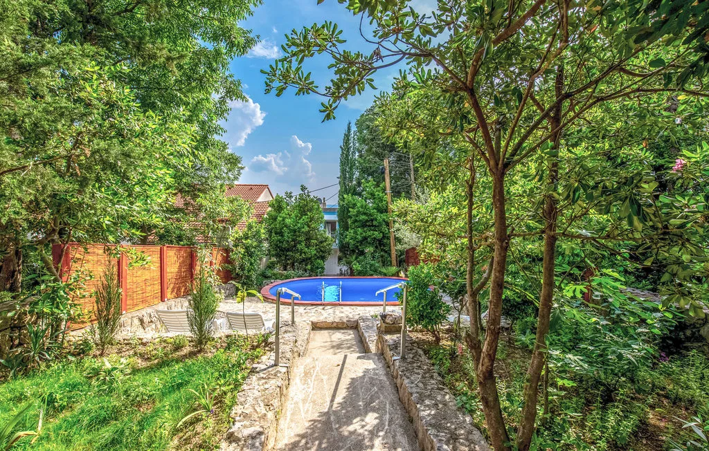 Un sendero del jardín conduce a una piscina azul rodeada de árboles y vegetación.