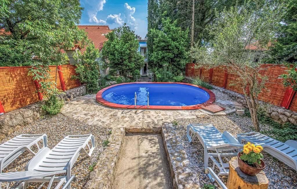 A small outdoor swimming pool is surrounded by stone paving and lounge chairs.