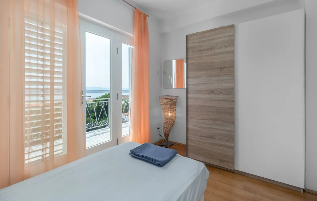 A bright bedroom with a bed beside a balcony door and orange curtains.