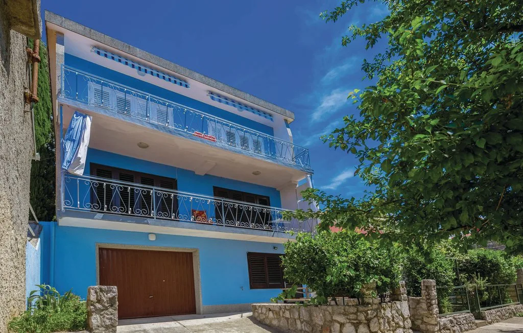 Casa azul de varias plantas con balcones y un árbol grande al lado.