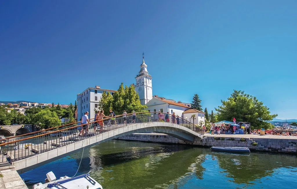 A pedestrian bridge crosses a river beside a waterfront town square.