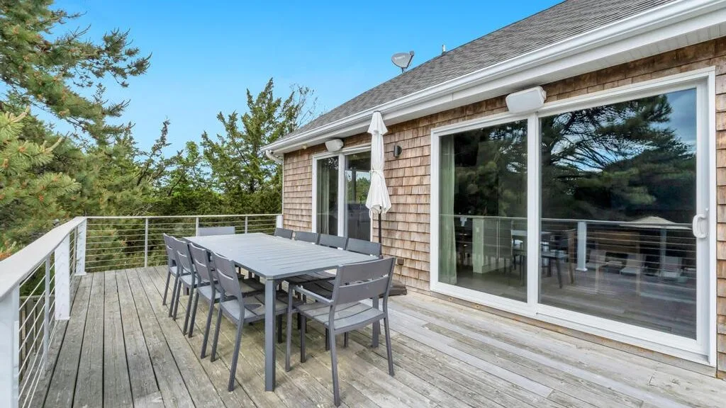 A spacious outdoor deck has a dining table and seating beside large glass doors.