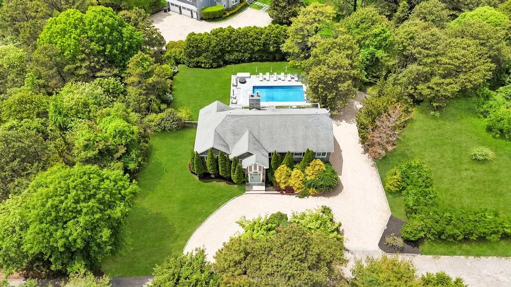 Aerial view of a house surrounded by trees, with a swimming pool behind it.