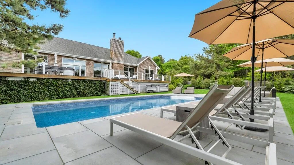 An outdoor swimming pool beside a house, with loungers and patio umbrellas.