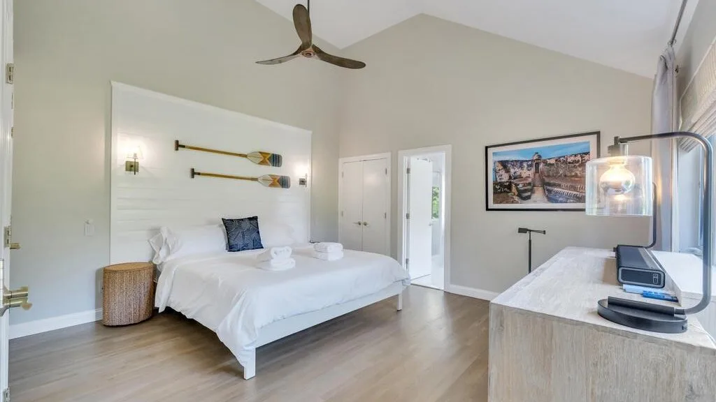 A bright bedroom with a large bed, wall art, and a ceiling fan.