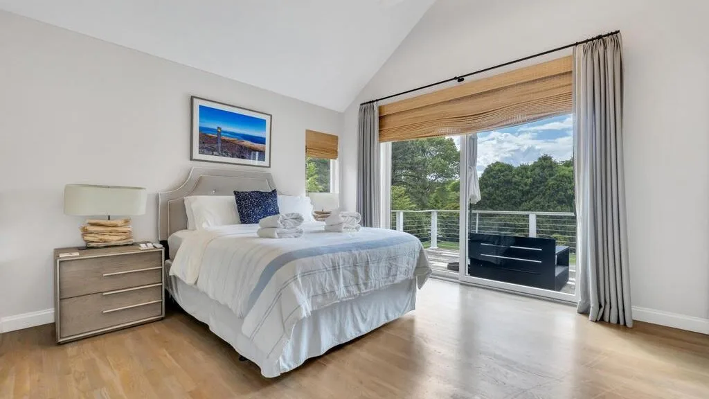 A bright bedroom with a neatly made bed beside large glass doors opening to a balcony.