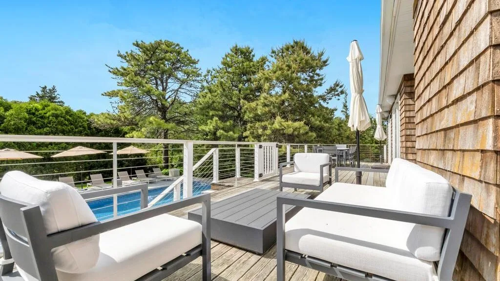 A sunny outdoor deck with cushioned seating, a table, and a pool.