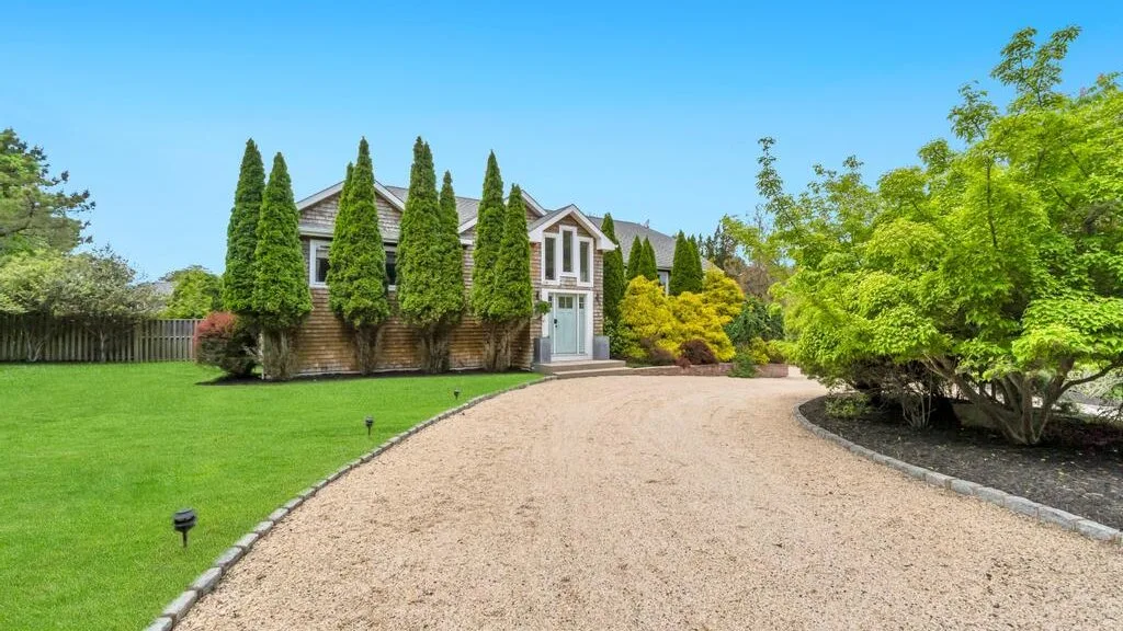 A landscaped house entrance beside a curved gravel driveway and green lawn.