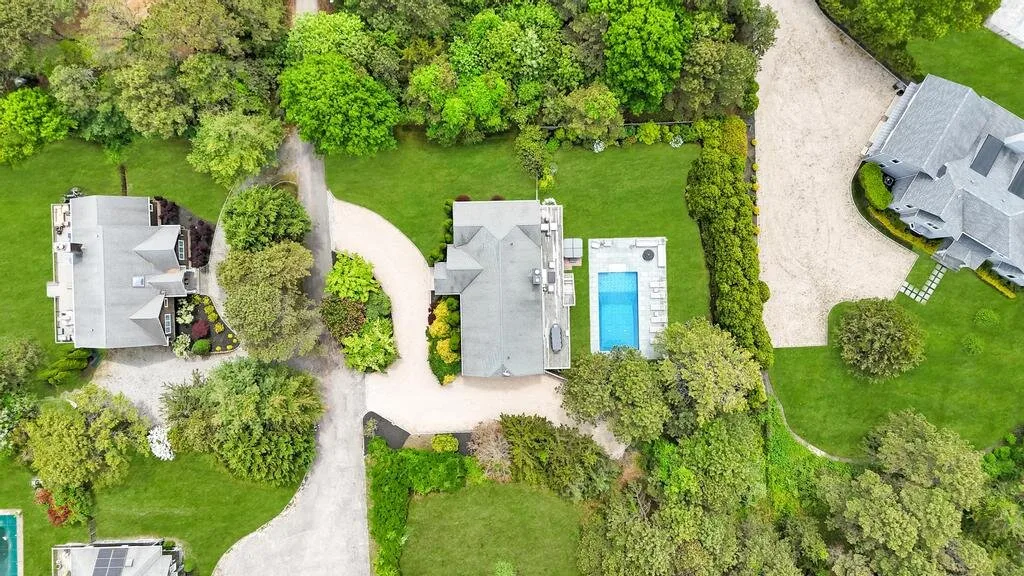 An aerial view of a landscaped property with houses, trees, and a swimming pool.