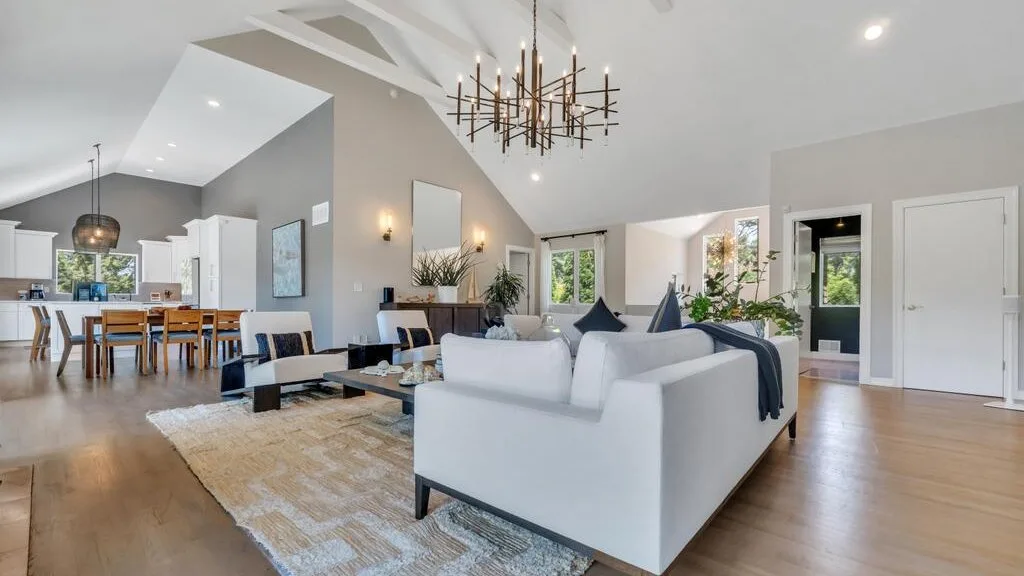 A bright open-plan living and dining area with seating beneath a high, angled ceiling.