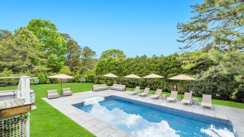 An outdoor swimming pool is surrounded by lounge seating and green lawn.