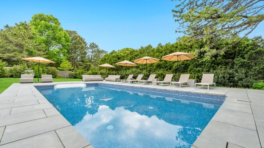 An outdoor swimming pool is surrounded by lounge seating and greenery.