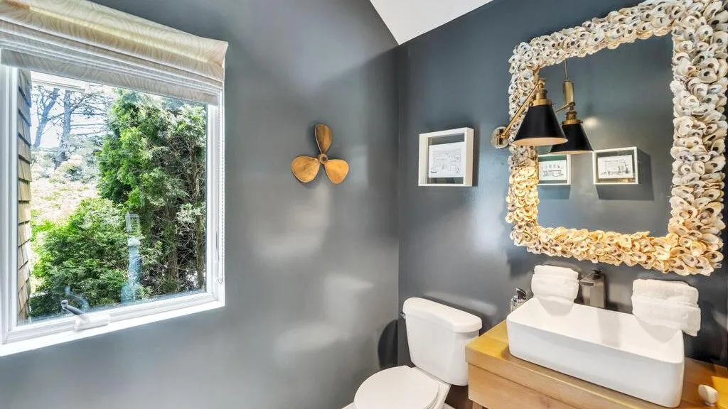 A bathroom with a vessel sink, wall mirror, and window overlooking greenery.