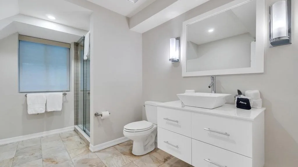 A bright bathroom with a vanity, mirror, toilet, and glass shower.