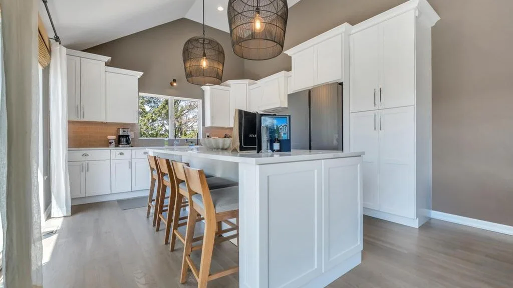 A bright kitchen with a central island, bar stools, and white cabinetry.