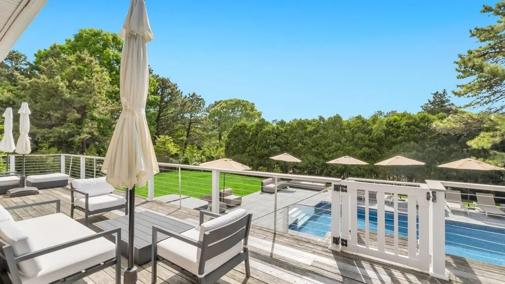 A sunny outdoor terrace overlooks a swimming pool and green trees.
