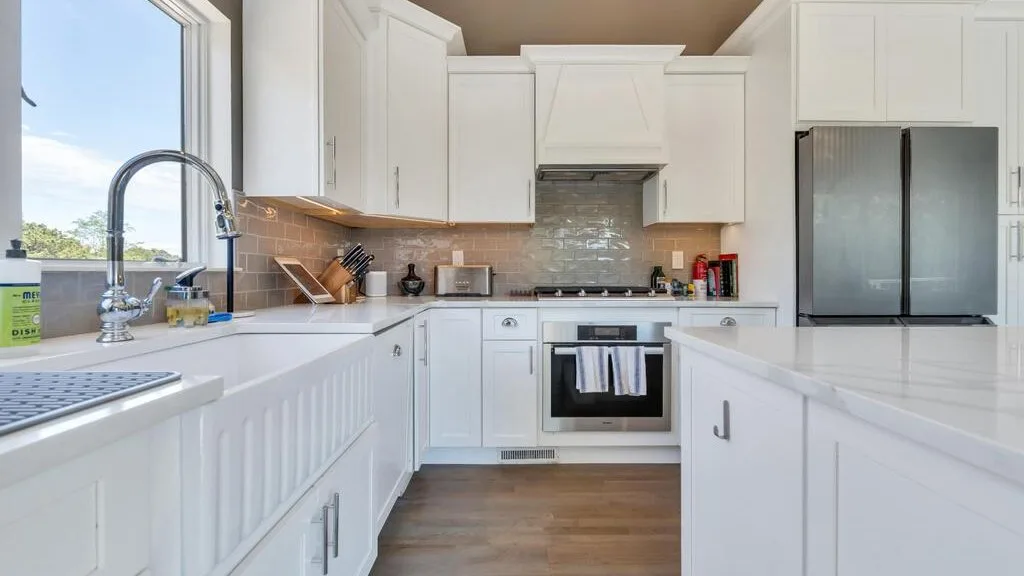 A bright white kitchen with a central island and stainless steel appliances.
