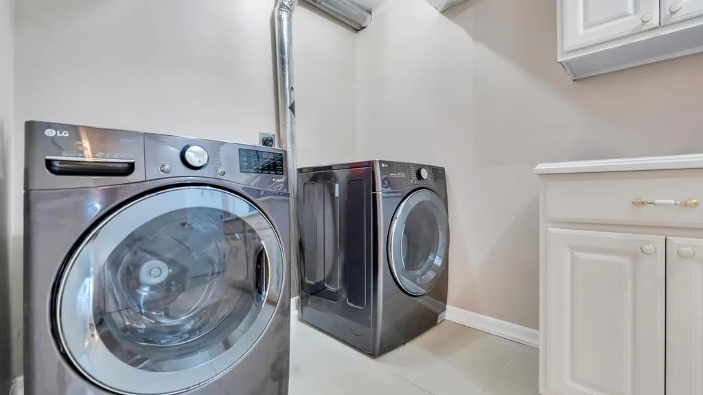 A laundry room with a front-loading washer and dryer beside white cabinets.