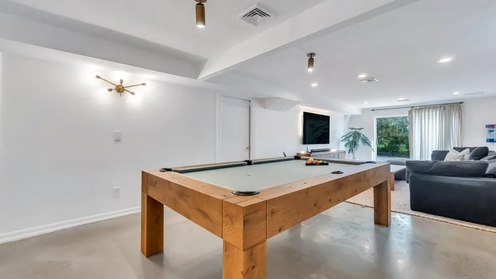 A recreation room with a pool table and seating near the windows.
