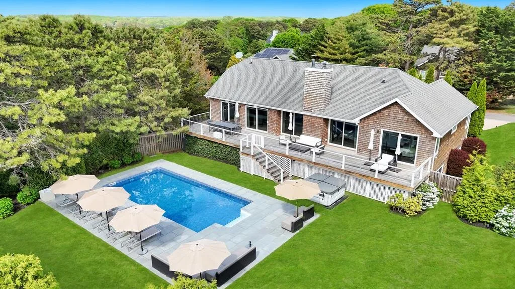 A brick house overlooks a backyard pool and patio surrounded by green lawn.