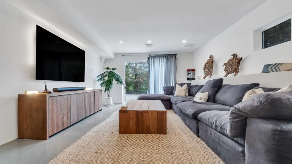A bright living room with gray seating, a wooden coffee table, and a wall-mounted television.