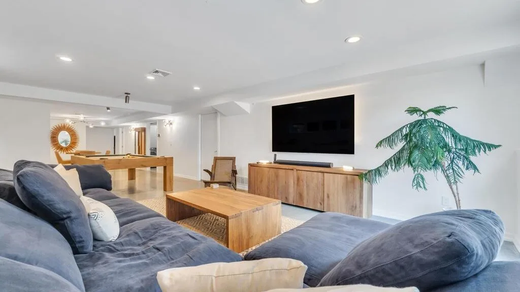 A bright living room with gray seating, a wooden coffee table, and a wall-mounted television.