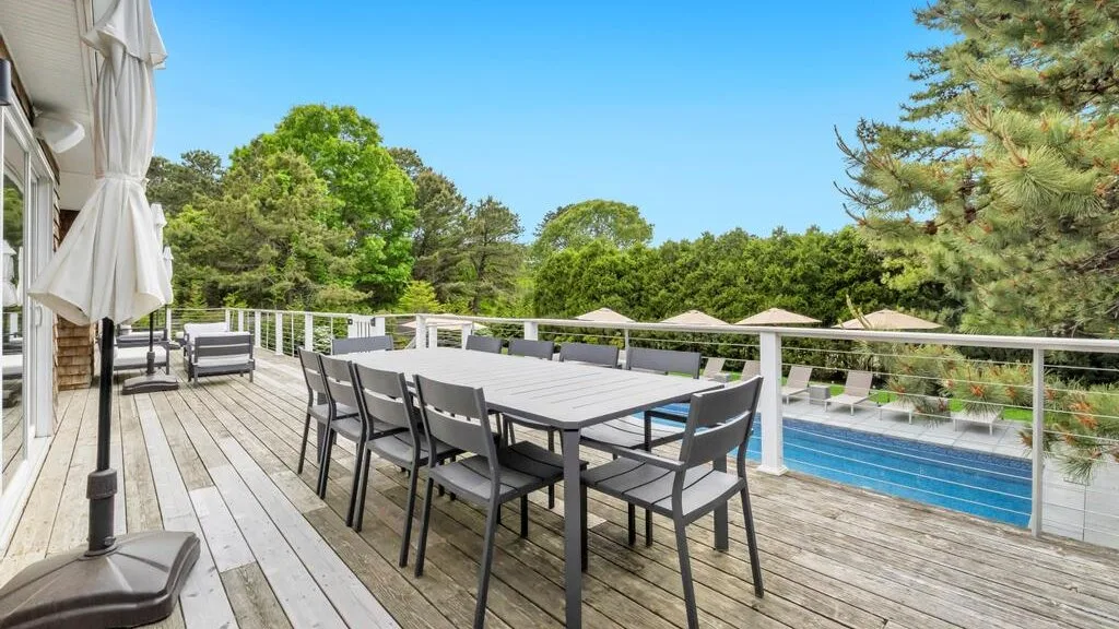A spacious outdoor dining deck overlooks a swimming pool and surrounding trees.