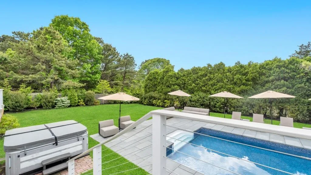 An outdoor swimming pool and hot tub sit beside a green lawn and trees.