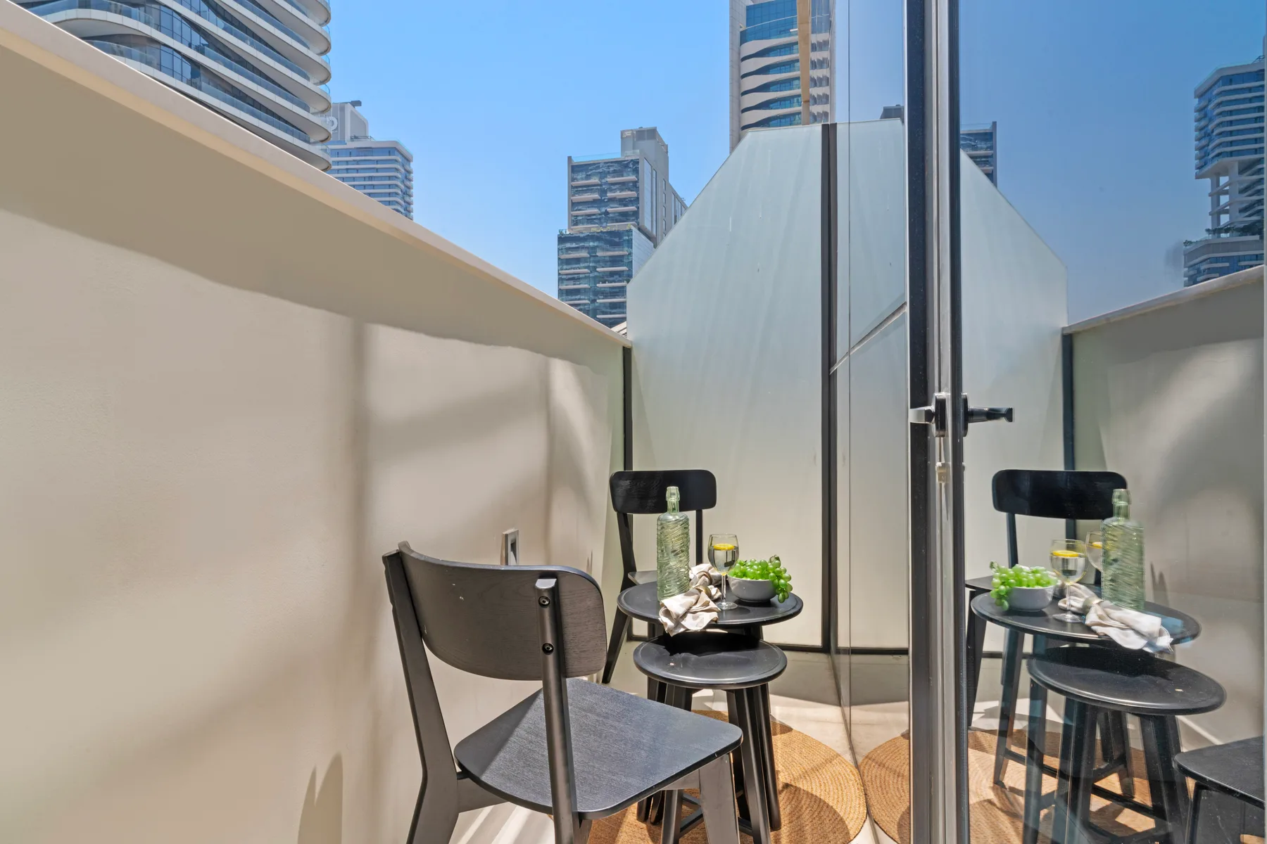 Un pequeño espacio de estar en un balcón con una mesa y vistas a edificios altos cercanos.