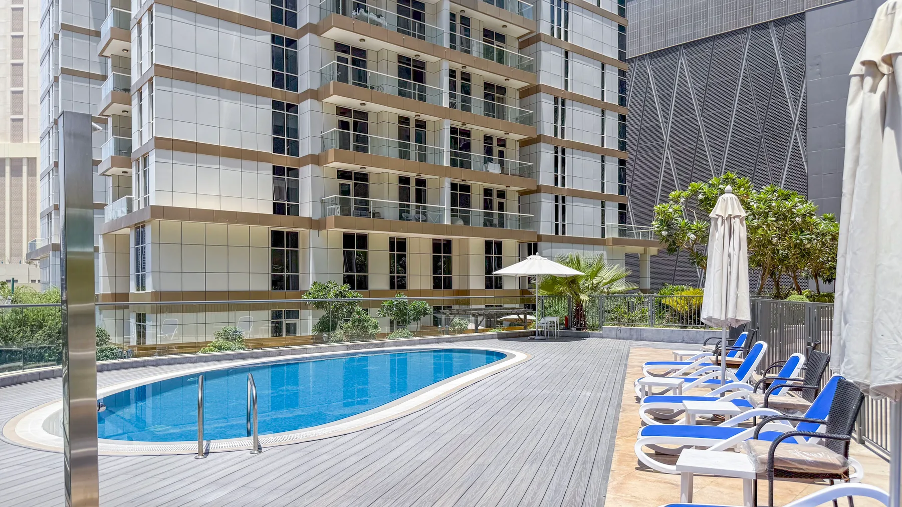 Una terraza con piscina tiene asientos y sombrillas junto a un edificio alto.