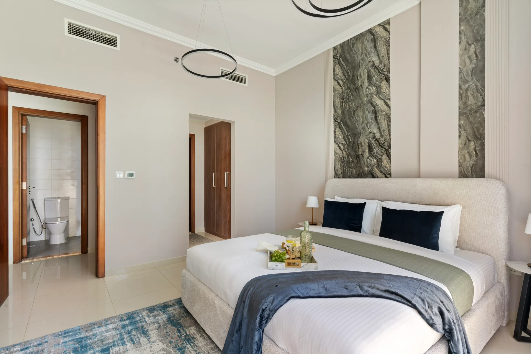 Un dormitorio con una cama grande, cojines oscuros y una alfombra azul.