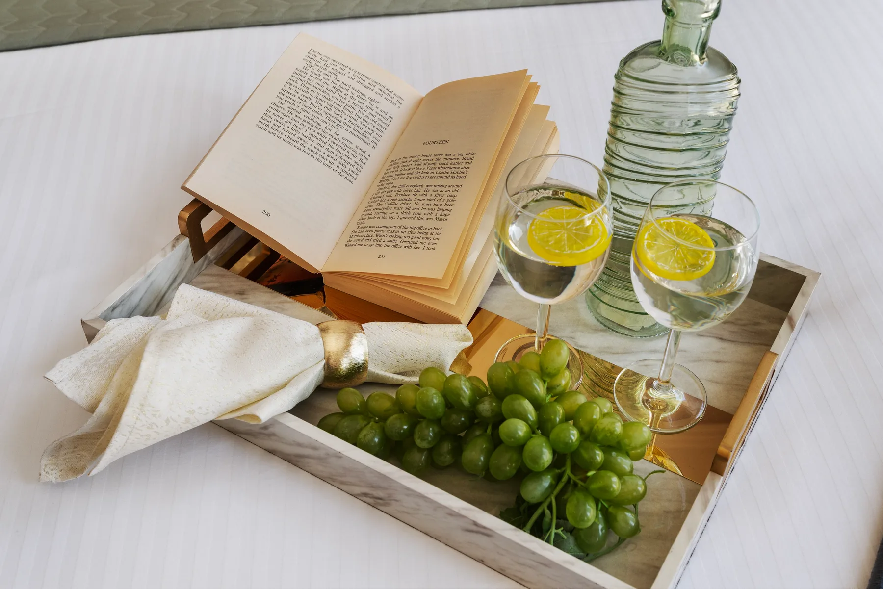 Un libro abierto y una bandeja con uvas, bebidas cítricas y una botella de vidrio.