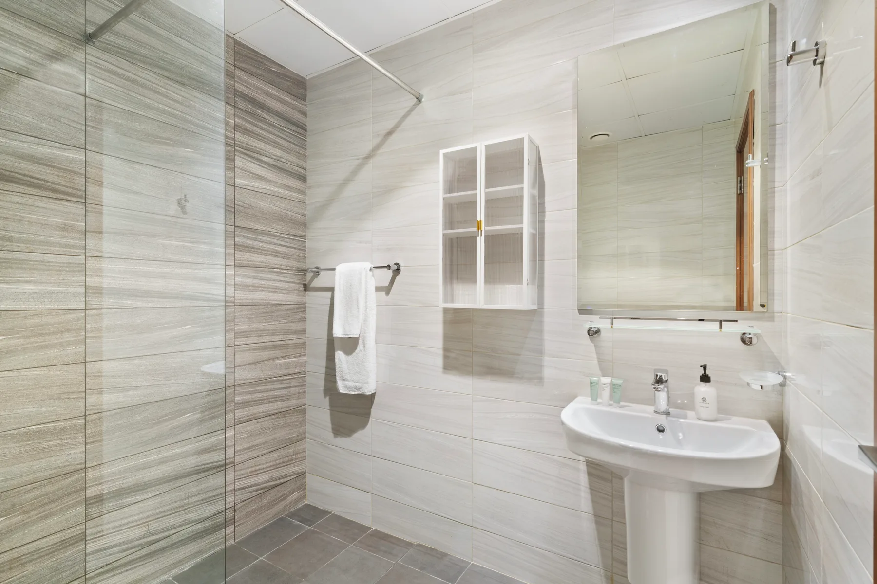 Un baño luminoso con azulejos, ducha de vidrio, lavabo y espejo.