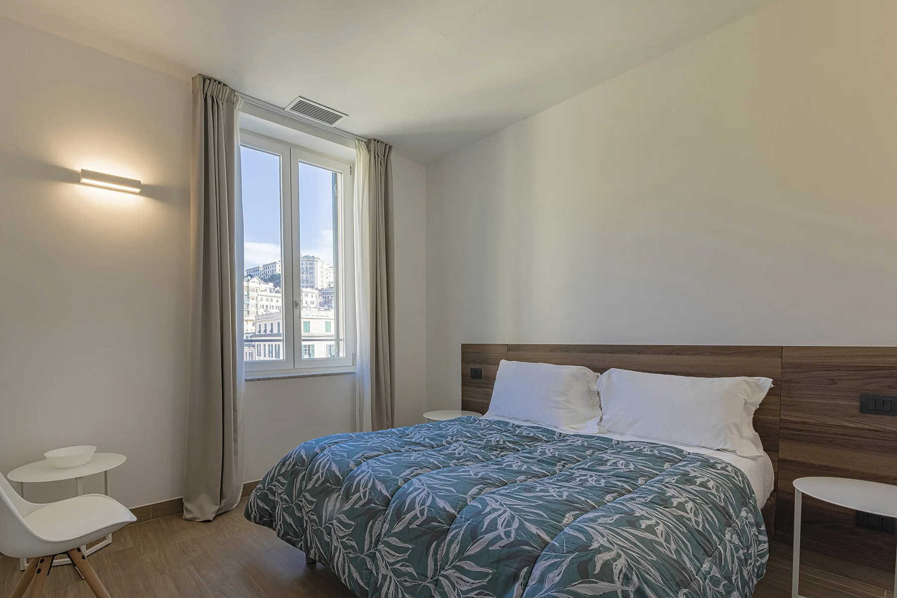 Un dormitorio con una cama, ropa de cama estampada y una ventana con cortinas.