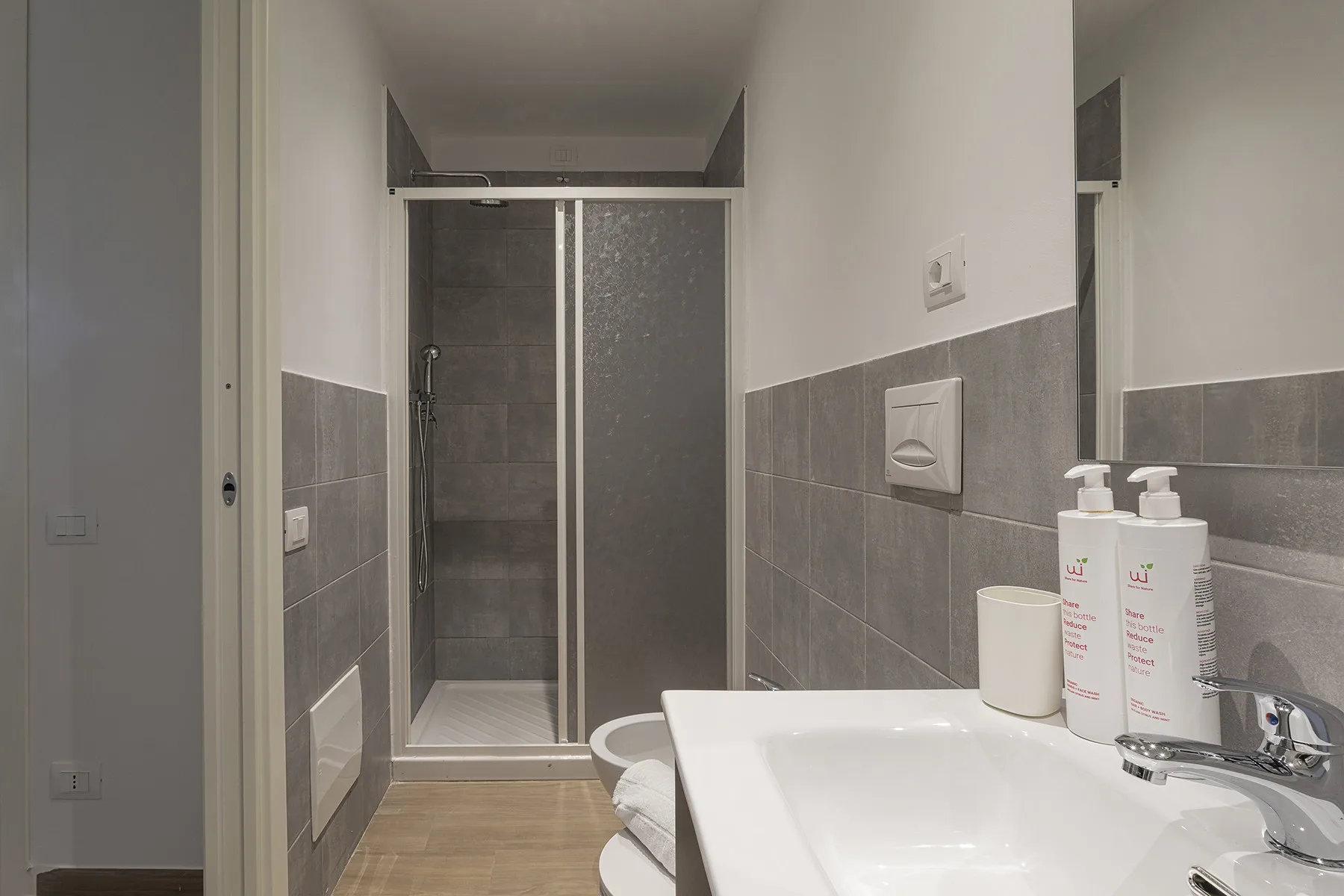 Un baño revestido de azulejos con ducha de vidrio y lavabo blanco.