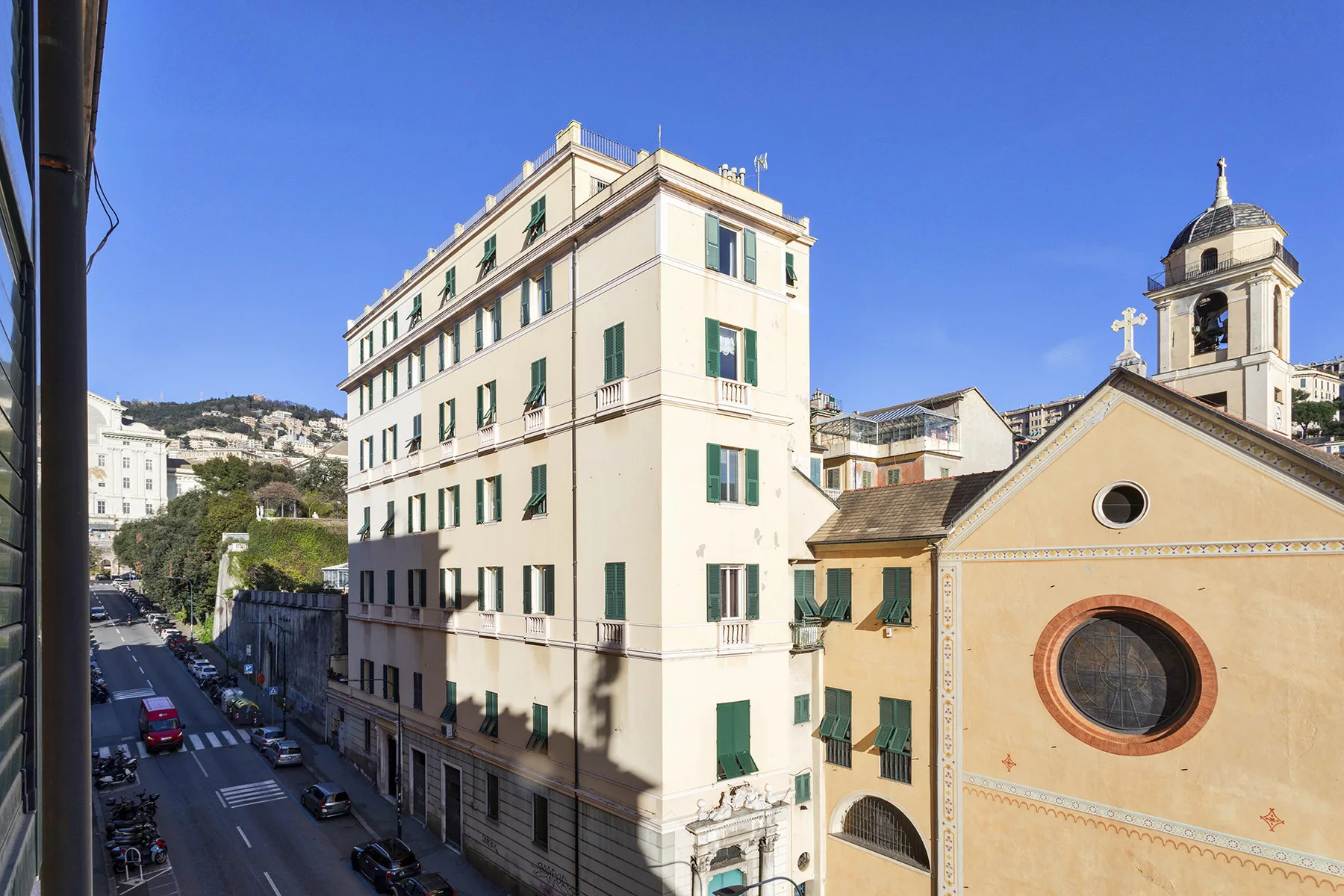 Una calle soleada bordea edificios claros y una iglesia con campanario.