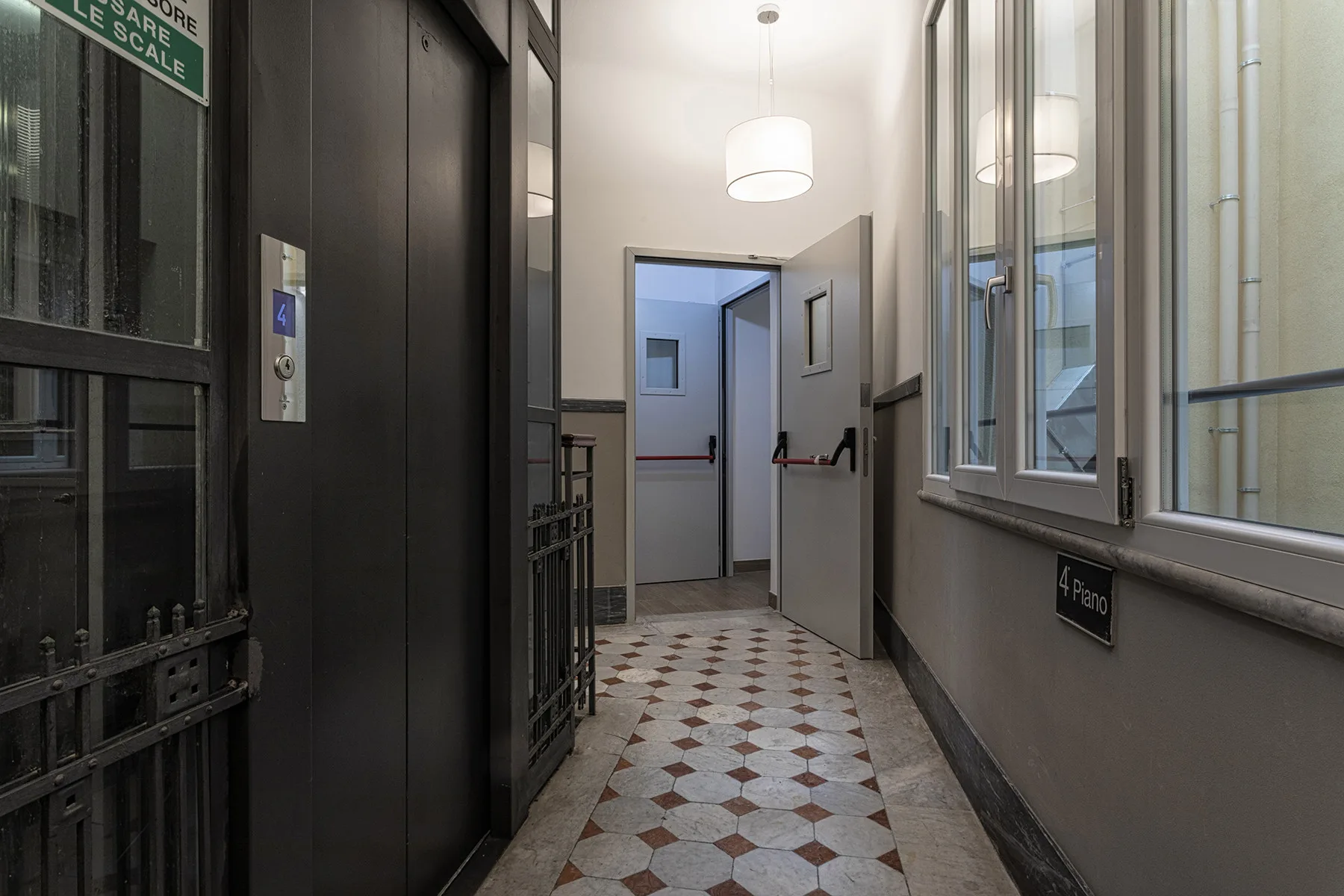 Un pasillo interior de baldosas conduce a una puerta abierta, con ventanas en una pared.