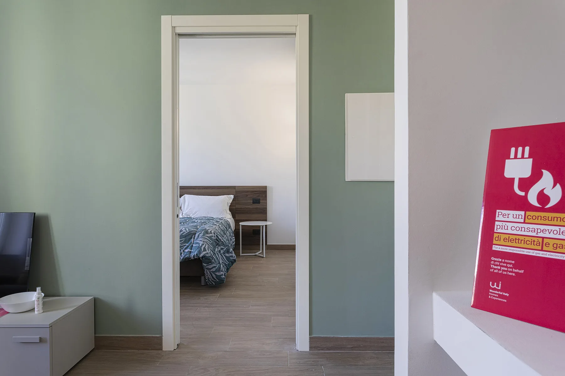 Se ve un dormitorio a través de una puerta, con una cama y una mesita de noche.