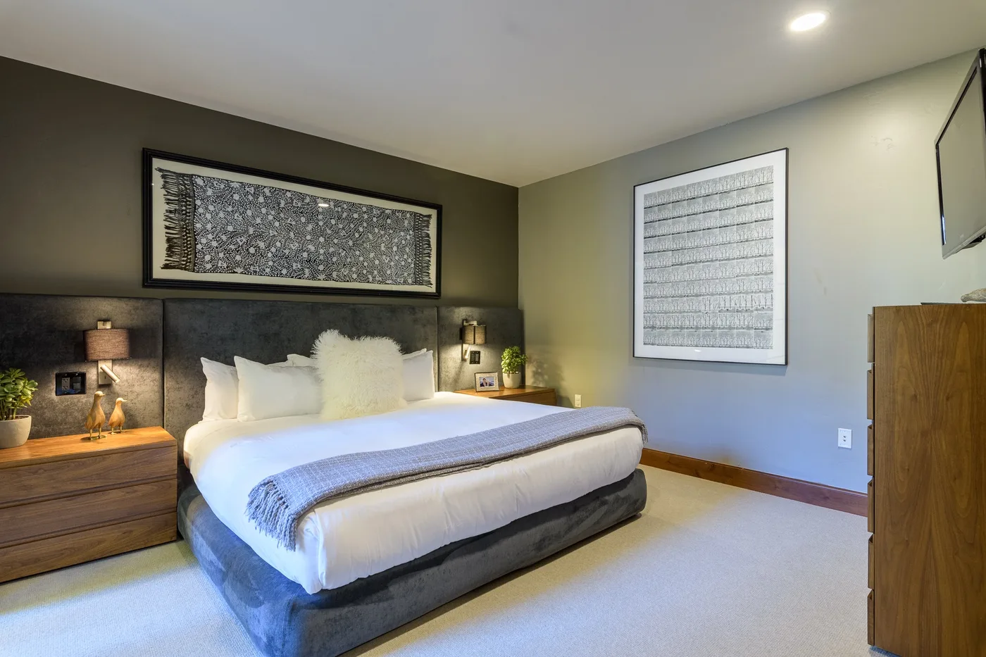 A bedroom with a large bed, framed artwork, and bedside tables.