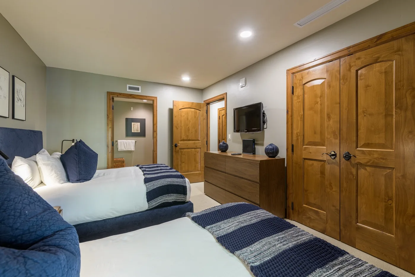 A bedroom with two beds, navy bedding, and wooden doors.
