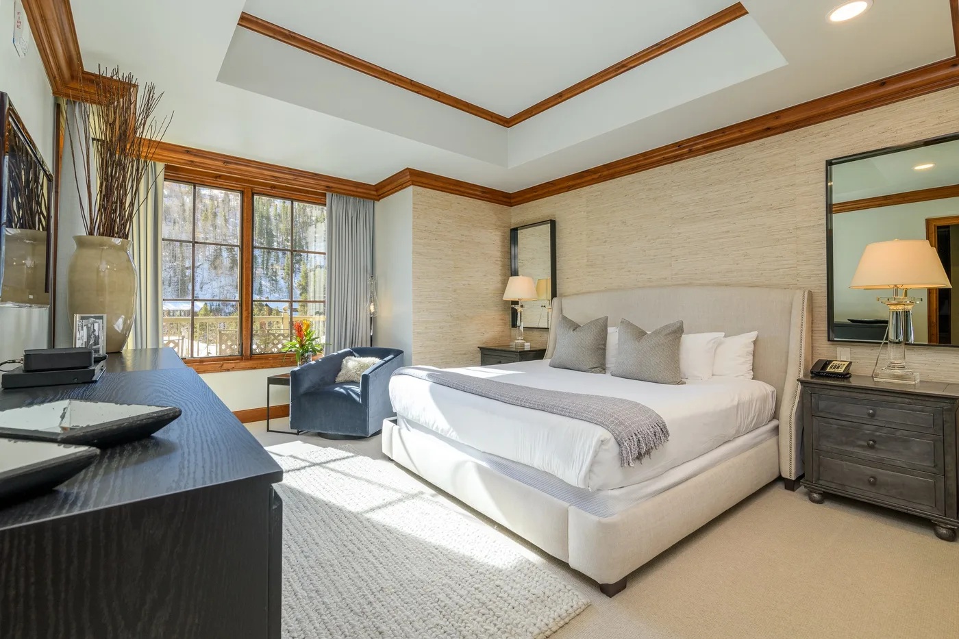 A bright bedroom with a large bed, a window, and a bedside table.