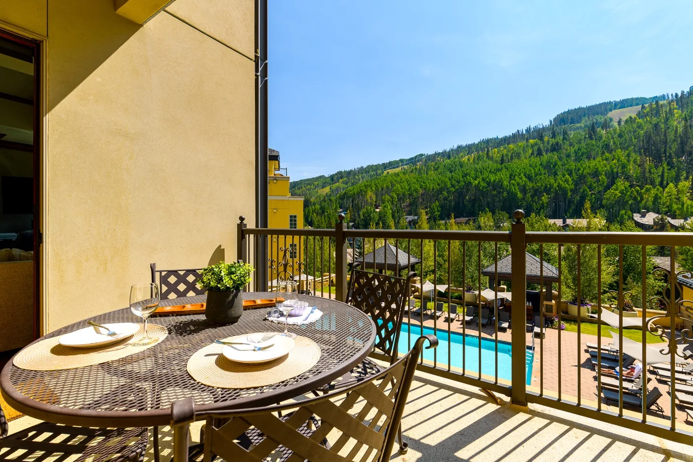 A balcony dining area overlooks a swimming pool and forested hillside.