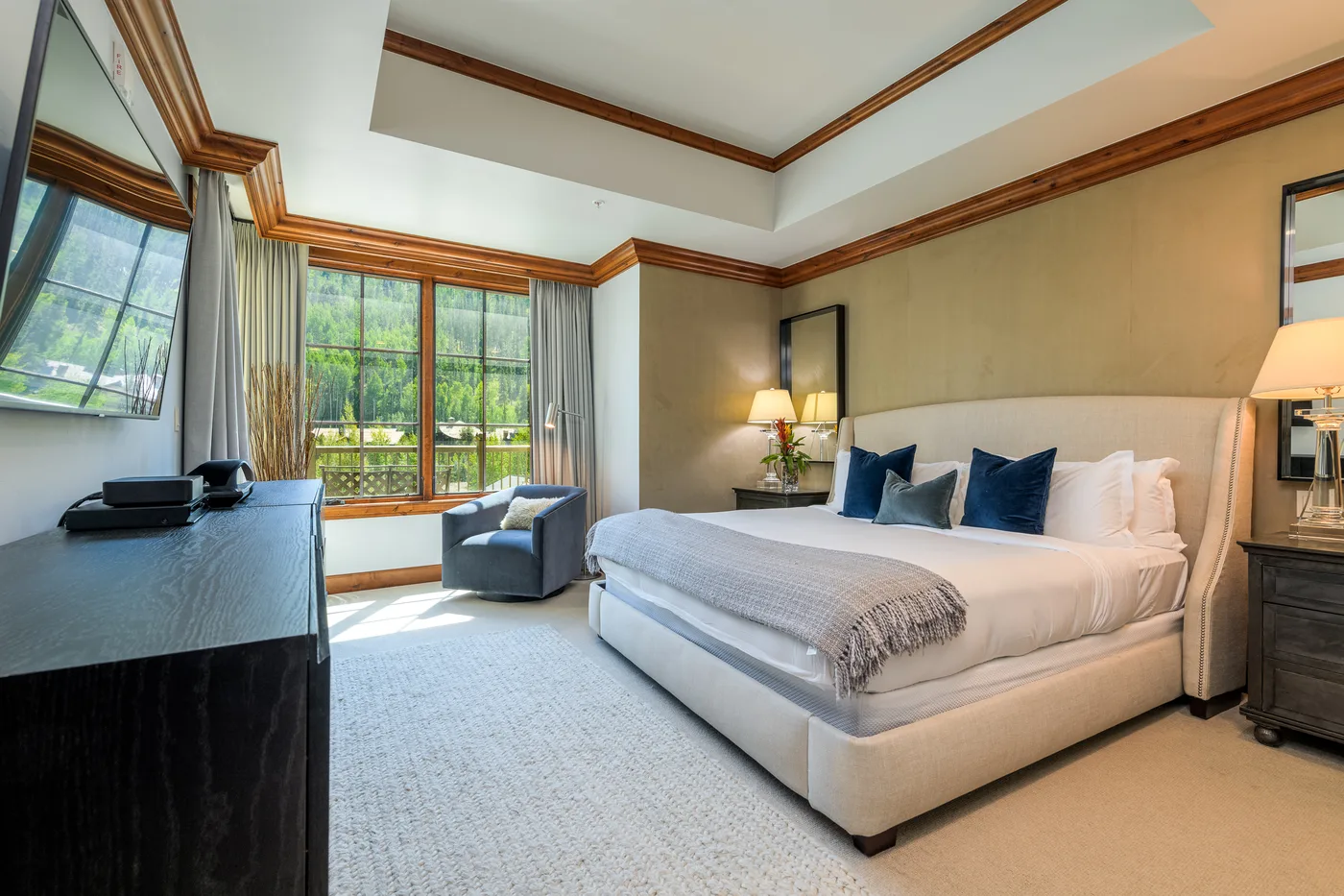 A bright bedroom with a large bed and windows overlooking greenery.
