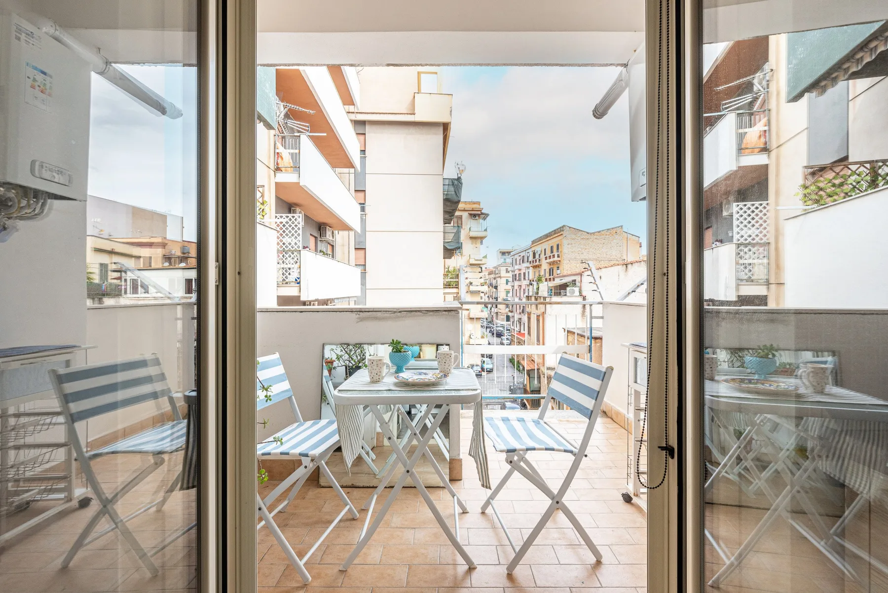 A balcony with a small table and folding chairs overlooks nearby buildings.