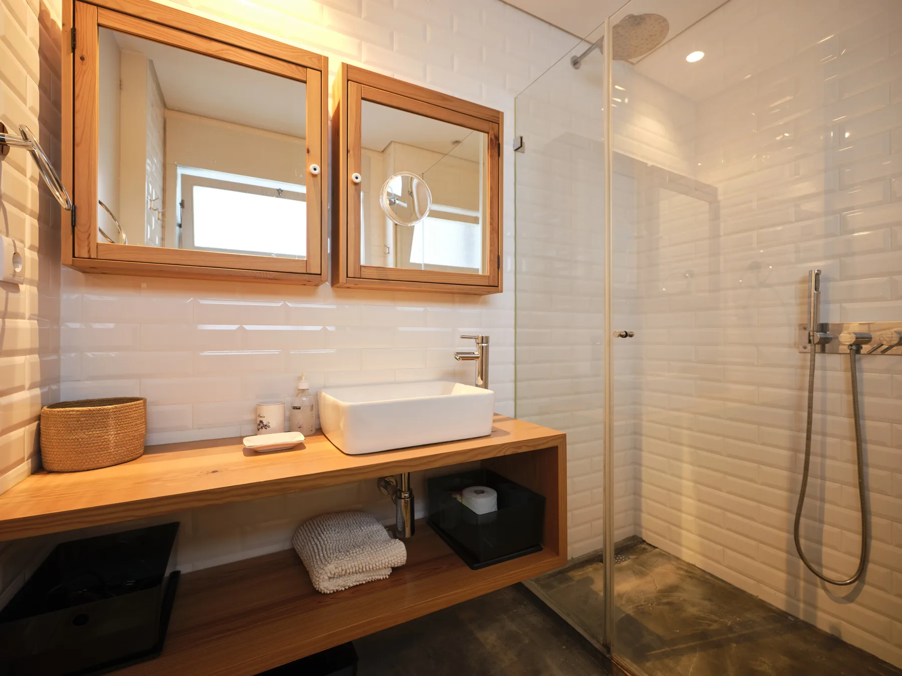A tiled bathroom with a wood vanity, basin, and glass shower.