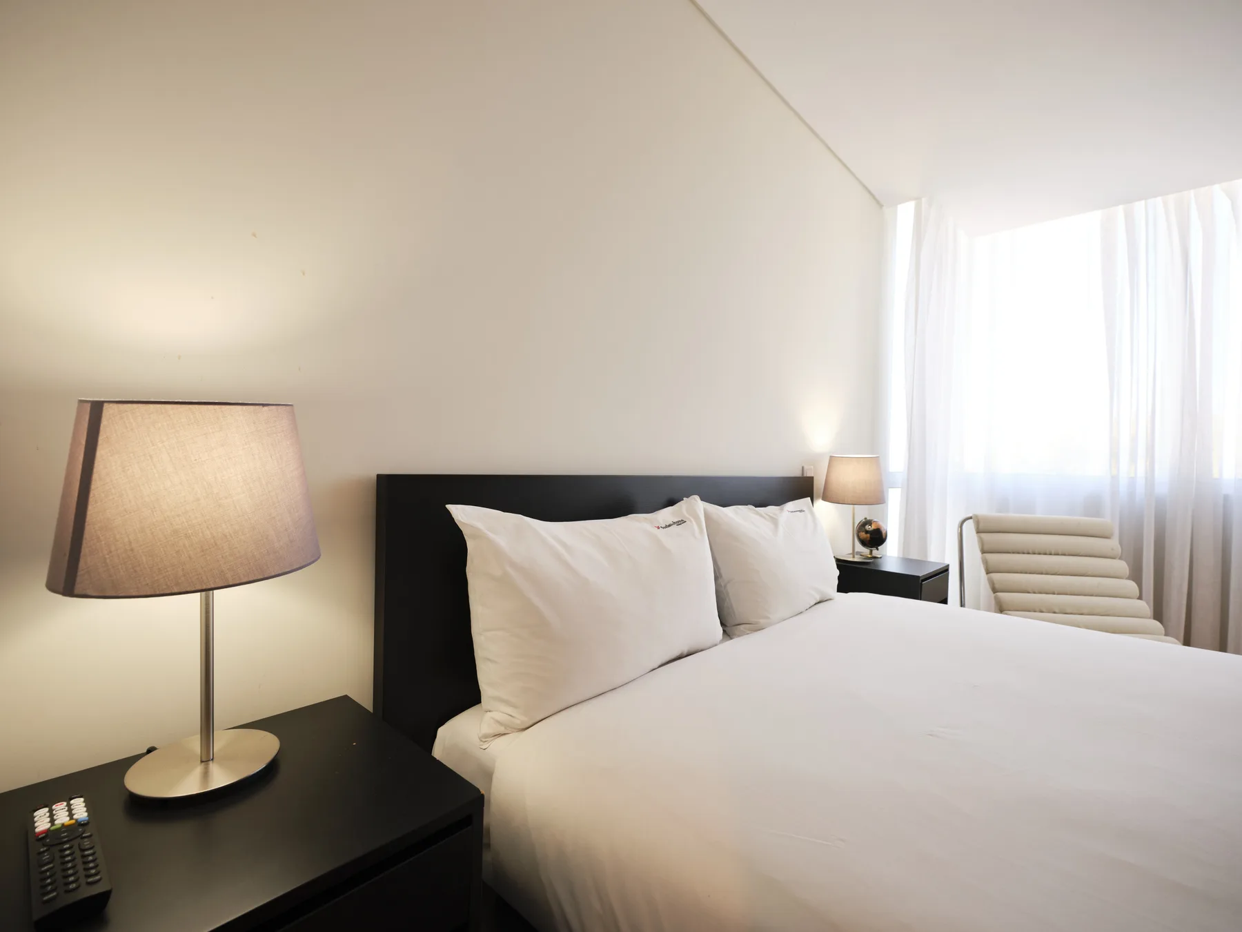 A bedroom with a neatly made bed beside a bedside table and lamp.