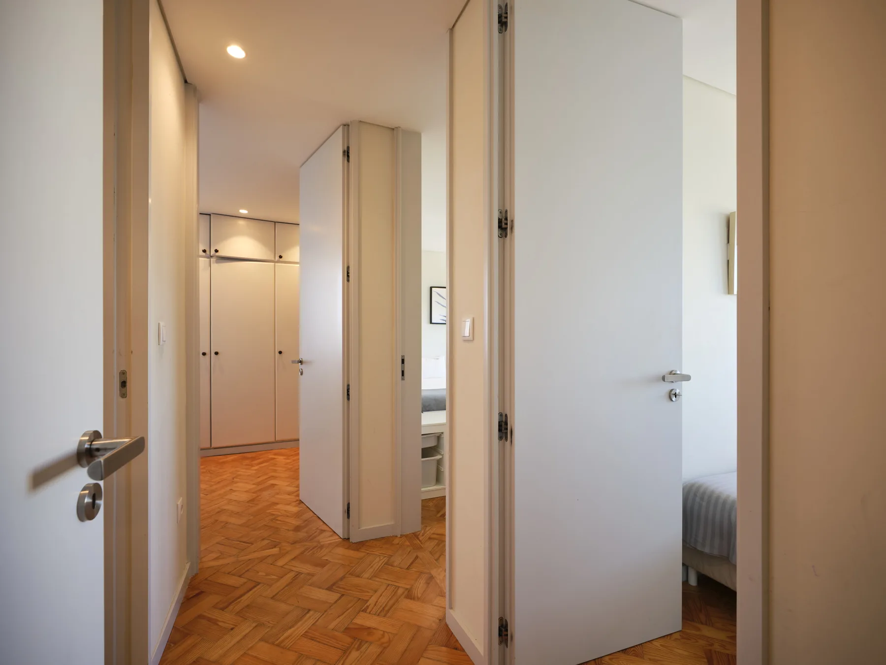 An apartment hallway with open doors and a glimpse of a bedroom.