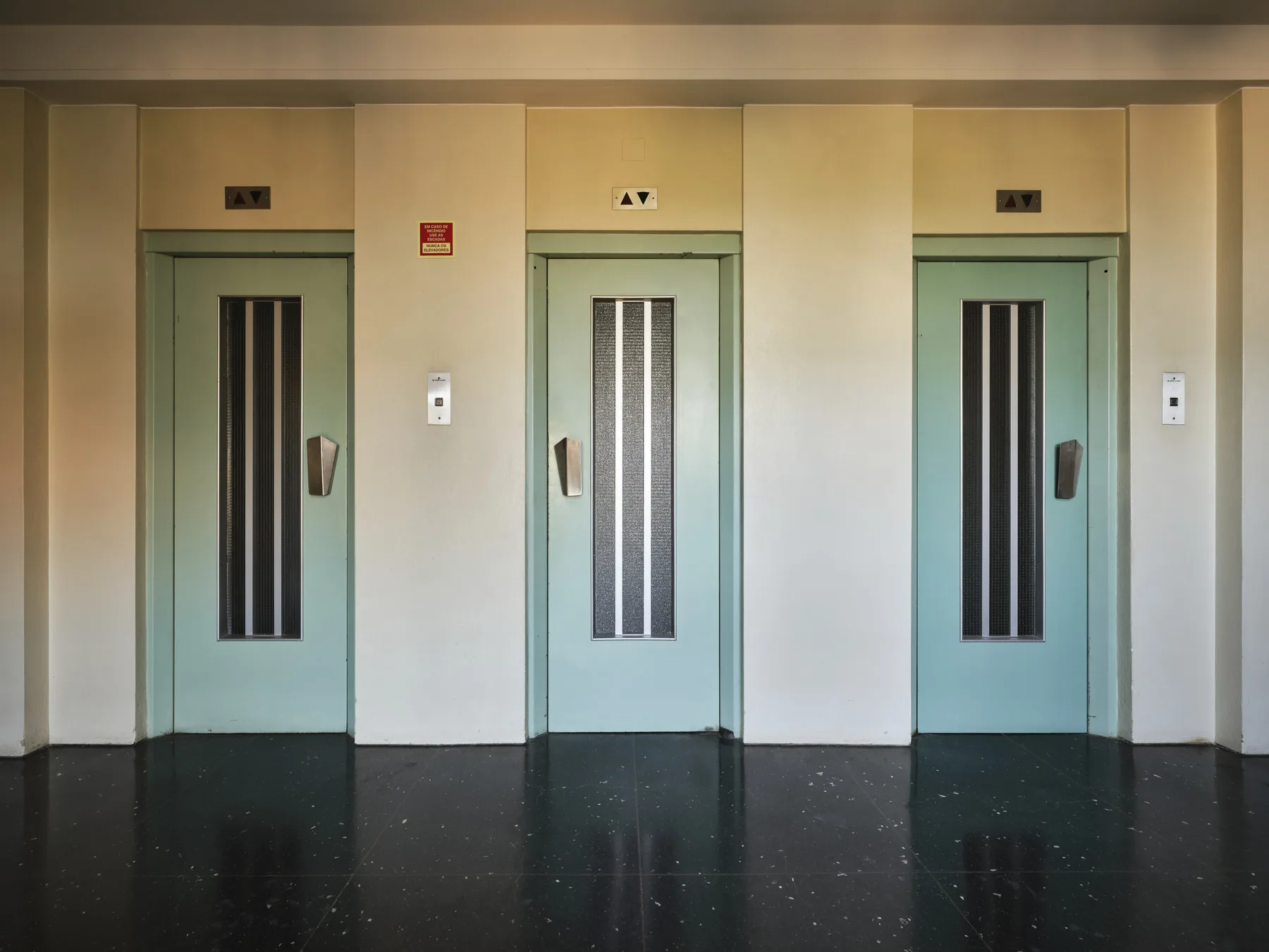 An elevator lobby with three elevator doors along a pale wall.