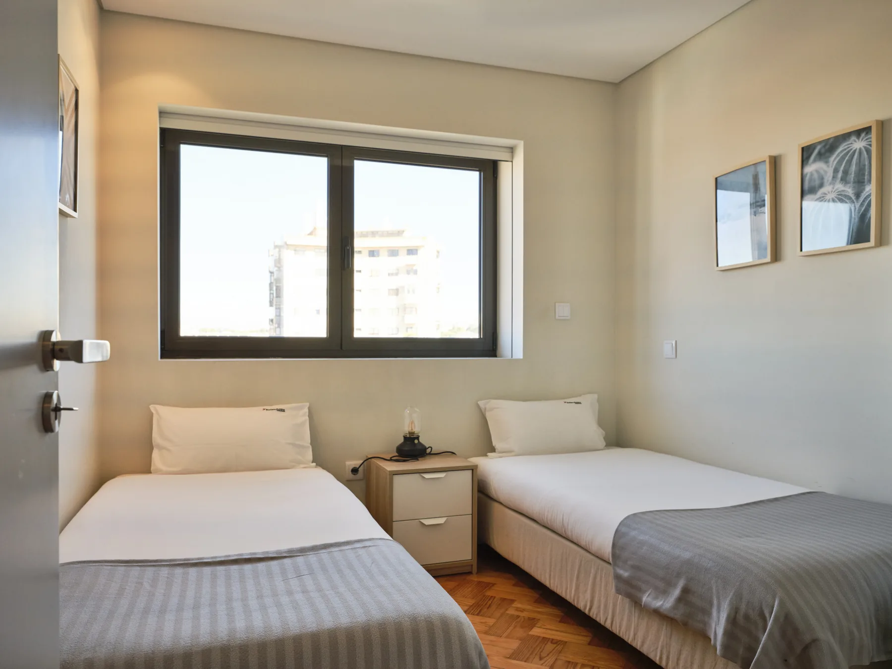 A bedroom with two beds and a window overlooking nearby buildings.