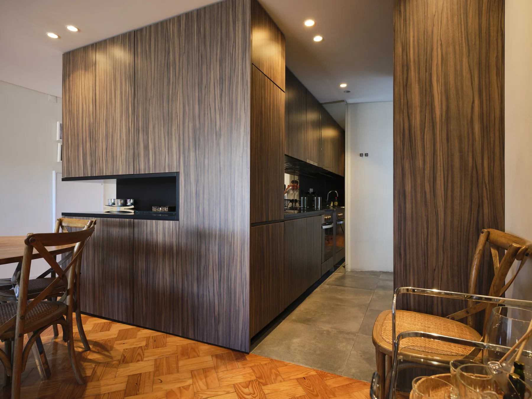 A dining area with wooden seating beside a modern kitchen and wood-paneled island.